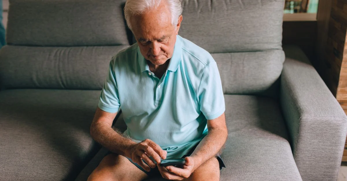 Homme senior assis sur un canapé utilisant un smartphone à la maison.