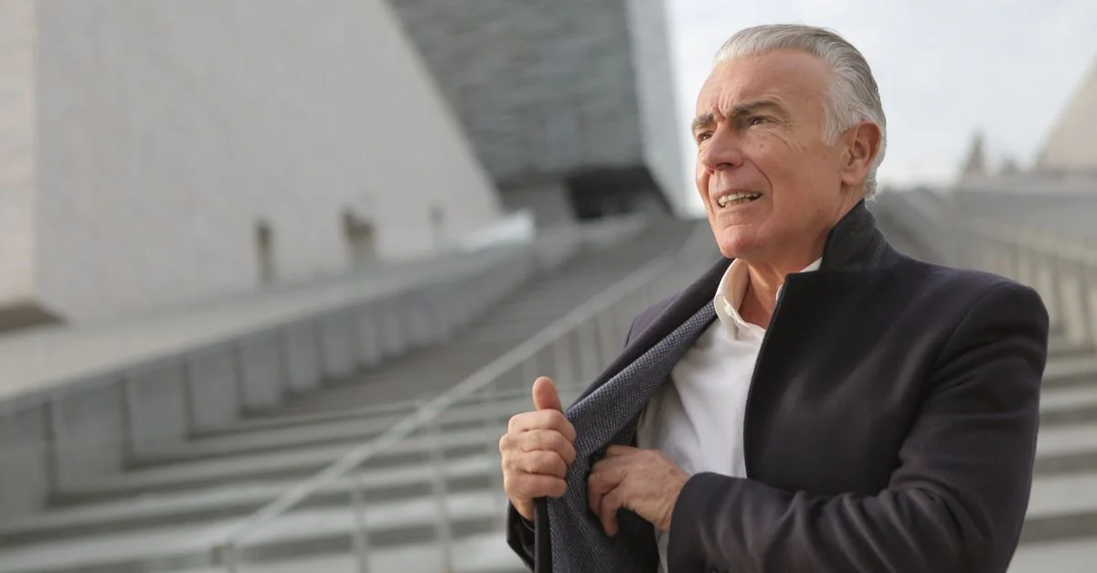 Homme senior ajustant son manteau debout sur un escalier urbain, dégageant confiance et style.
