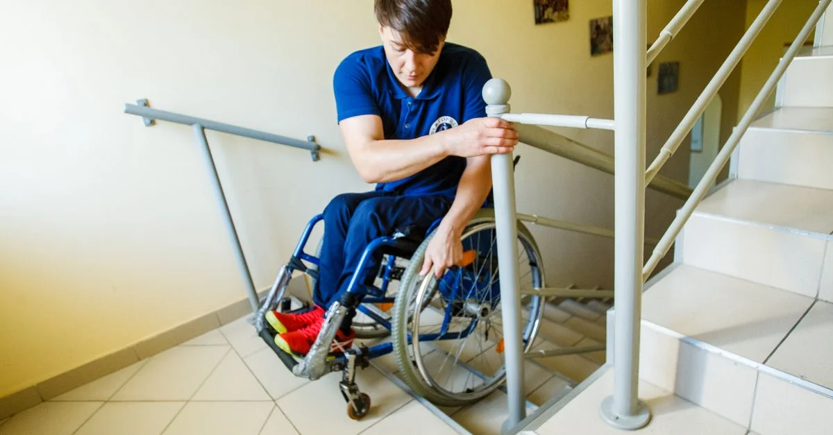 Un homme en fauteuil roulant utilisant la rampe d'escalier pour se soutenir à l'intérieur.