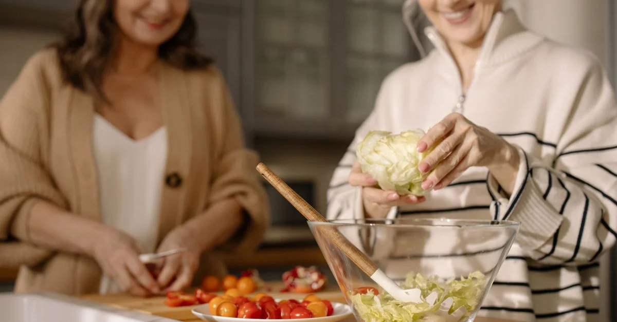 Une femme senior préparant joyeusement une salade fraîche avec des tomates cerises et de la laitue dans une cuisine cosy.
