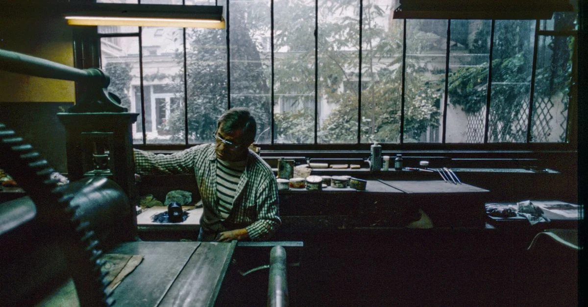 Un artisan utilisant une presse à imprimer vintage dans un atelier parisien, entouré d'outils et de matériaux.