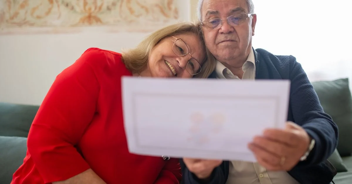 Un couple âgé examine joyeusement un document tout en étant assis confortablement ensemble sur un canapé.