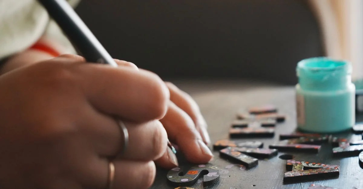 Des mains peignant des lettres en bois avec précision, montrant un projet créatif de bricolage.