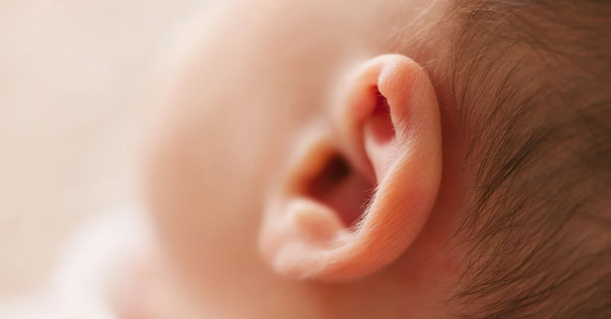 Gros plan doux de l'oreille d'un nouveau-né, mettant en valeur des caractéristiques délicates dans une image en flou doux.