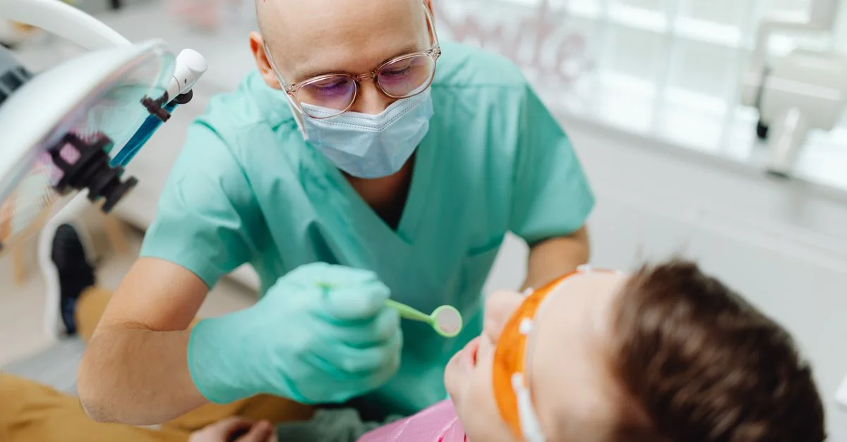 Dentiste en masque chirurgical examinant les dents d'un patient à l'aide d'outils dentaires.
