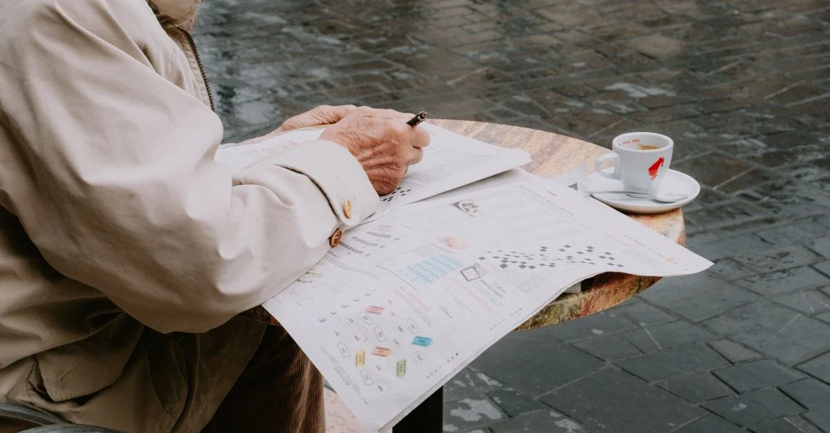 Un homme senior profite de son temps libre à résoudre un mots croisés dans un café en plein air.