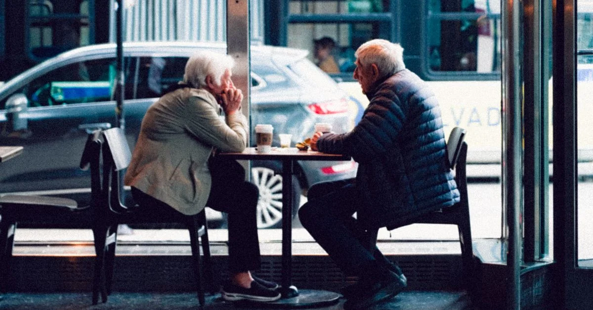 Un couple âgé partage un moment autour d'un café dans un cadre de café chaleureux.
