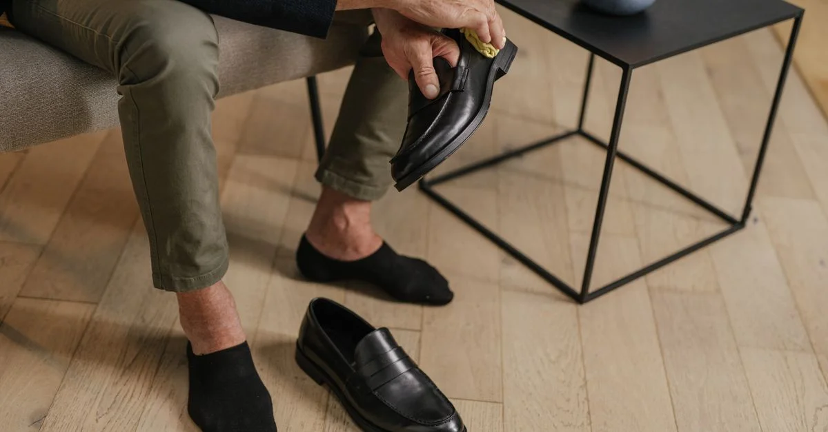 Un adulte senior polissant des chaussures en cuir noir à l'intérieur, montrant soin et routine.
