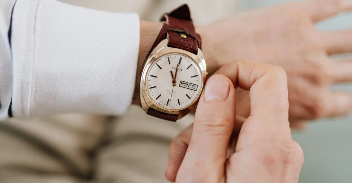 Gros plan sur une personne ajustant une montre-bracelet analogique vintage à bracelet en cuir brun.