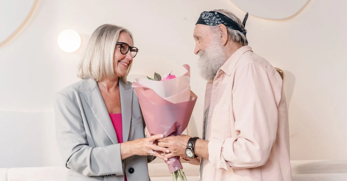 Moment charmant d'un couple âgé échangeant un bouquet à l'intérieur, mettant en valeur l'amour et la complicité.