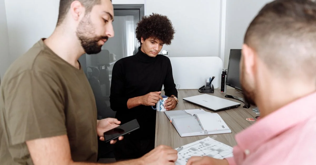 Trois collègues discutant de travail autour d'une table dans un cadre de bureau moderne.