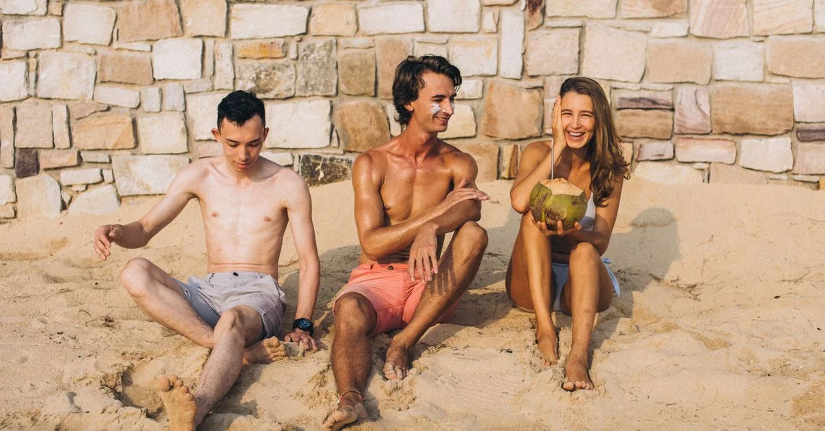 Trois amis se détendant sur une plage de sable, dégustant du jus de coco au soleil.