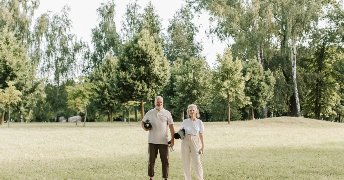 Couple âgé profitant d'un exercice en plein air tenant des tapis de yoga dans un parc ensoleillé et verdoyant.