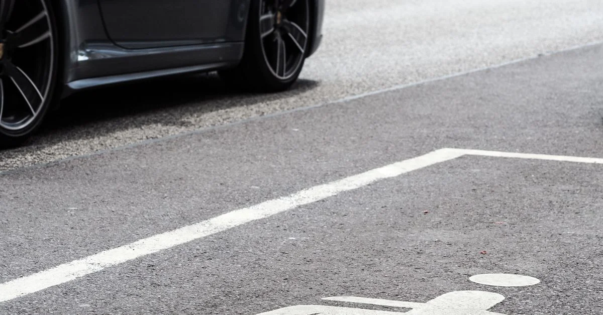 Un véhicule de luxe stationné dans une place de parking réservée aux personnes handicapées sur une rue urbaine.
