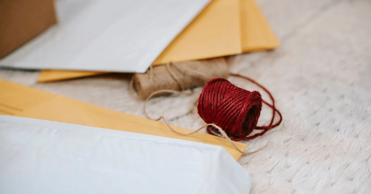 Enveloppes variées avec du fil rouge disposées sur une surface textile douce, idéales pour des thèmes de papeterie.