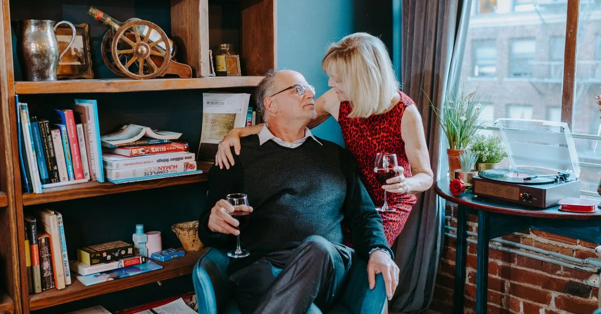 Un couple senior partage un moment affectueux avec du vin, entouré de livres et de musique.