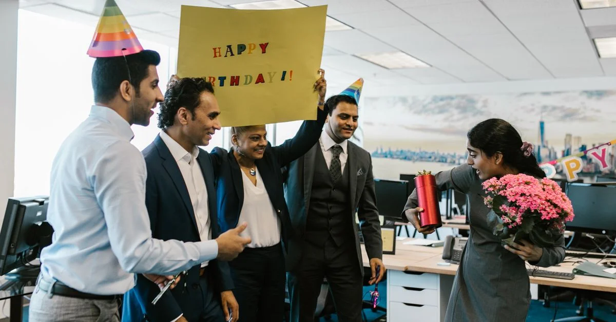 Des collègues surprennent un colaborateur avec une célébration d'anniversaire dans un bureau moderne.