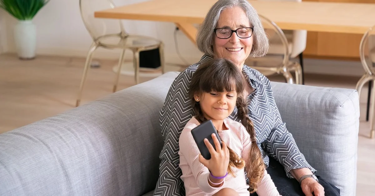 Une grand-mère et son petit-enfant partagent un moment joyeux en prenant un selfie à l'intérieur.