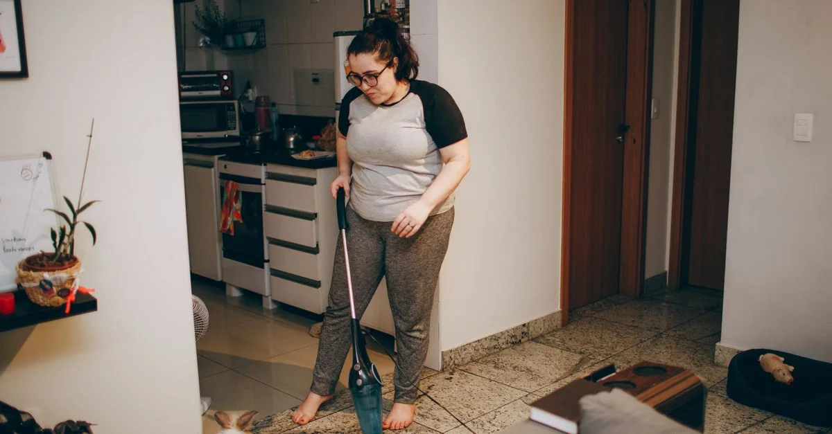 Une femme nettoie son salon avec un aspirateur pendant que son lapin de compagnie regarde.