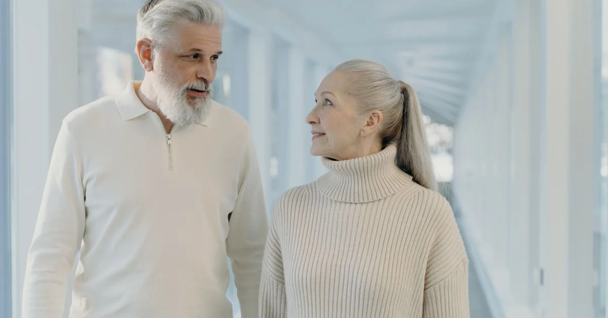 Un couple mature marchant et discutant dans un couloir lumineux.