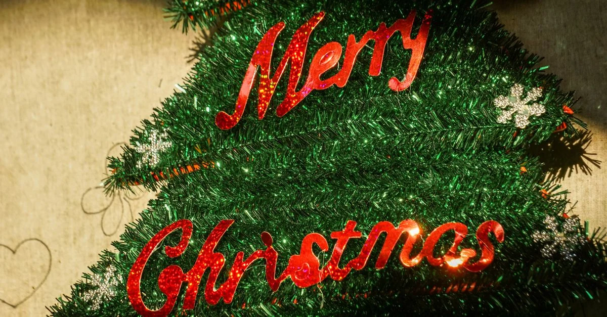 Sapin de Noël décoratif orné d'une joyeuse pancarte « Joyeux Noël » en lettres rouges scintillantes.