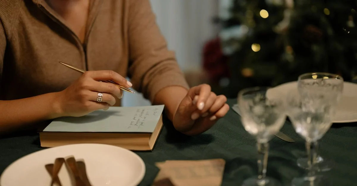 Femme tenant un stylo, écrivant une lettre sur une table préparée pour le dîner de Noël.