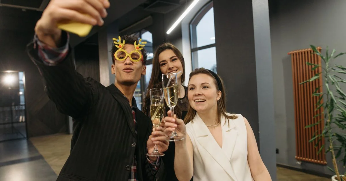 Groupe de collègues prenant un selfie lors d'une fête de bureau festive célébrant avec du champagne.