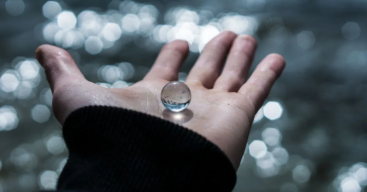 Un gros plan d'une main tenant une marbre en verre avec un beau fond bokeh flou.
