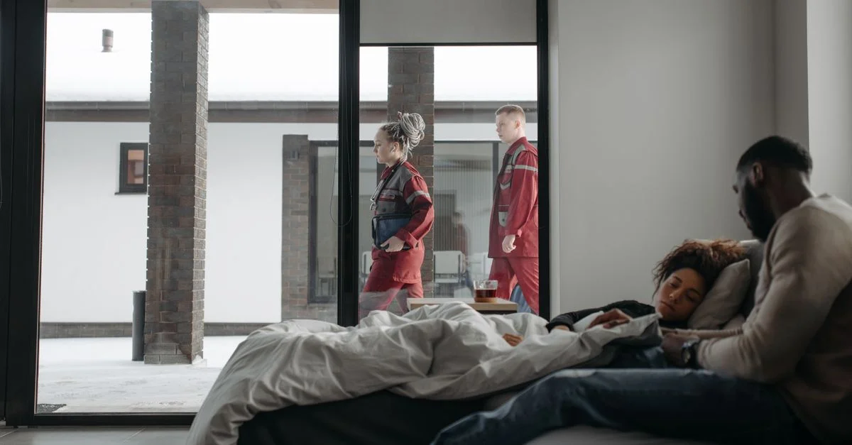 Des sauveteurs aident une femme à domicile tandis que son partenaire la réconforte, soulignant le soutien médical.