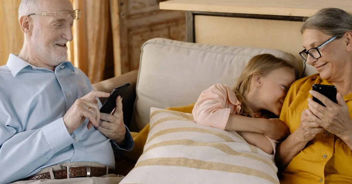Un moment familial chaleureux avec des grands-parents et leur petite-fille utilisant des smartphones sur un canapé douillet.