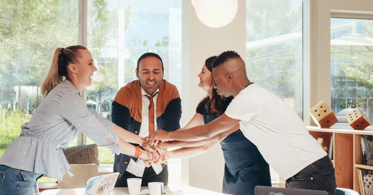 Un groupe diversifié de professionnels se tient la main dans un environnement de bureau moderne, montrant l'unité et le travail d'équipe.