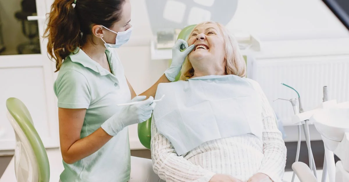 Une dentiste examine une femme âgée dans un cabinet dentaire. Toutes deux sourient.