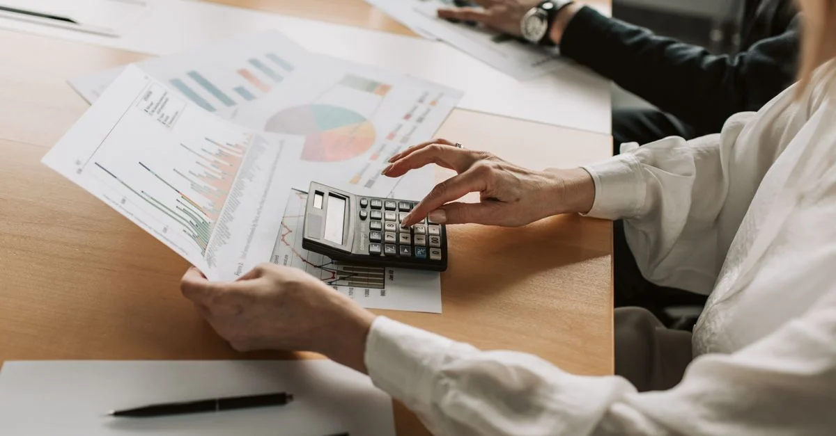 Mains effectuant des calculs financiers avec des graphiques et une calculatrice à une table de réunion.