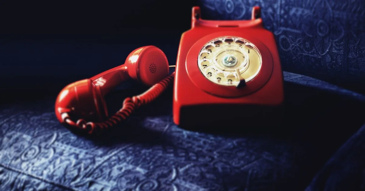 Un téléphone rotatif rouge classique posé sur un élégant tissu bleu texturé, évoquant la nostalgie.