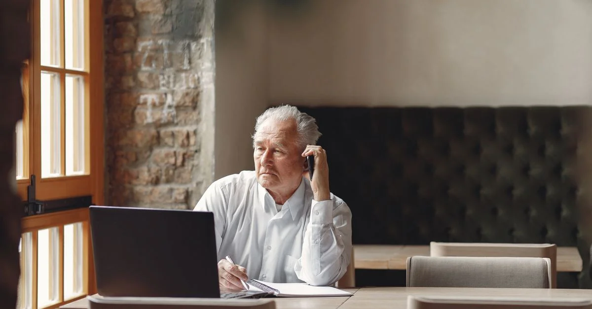 Homme d'affaires senior passant un appel tout en utilisant un ordinateur portable dans un cadre de bureau.