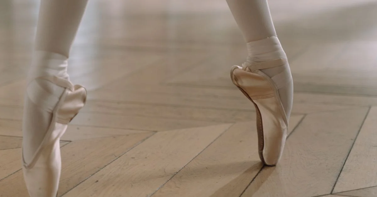 Gros plan des pieds d'une ballerine en pointes, montrant grâce et équilibre sur un sol en bois.