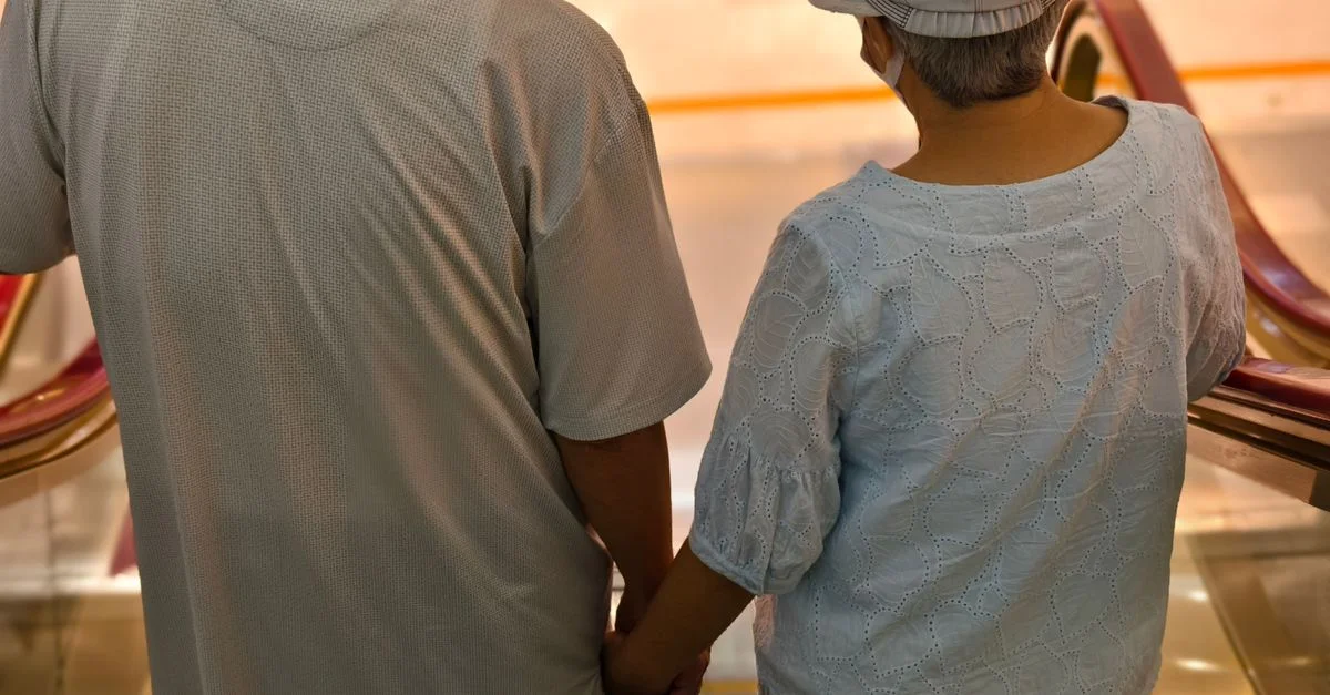 Un couple de personnes âgées descend l'escalator main dans la main, symbolisant un amour éternel.