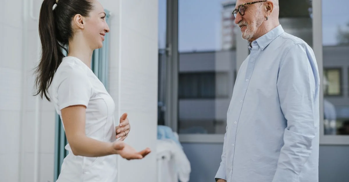 Une infirmière et un patient âgé partagent un moment léger lors d'un rendez-vous de santé à l'intérieur.
