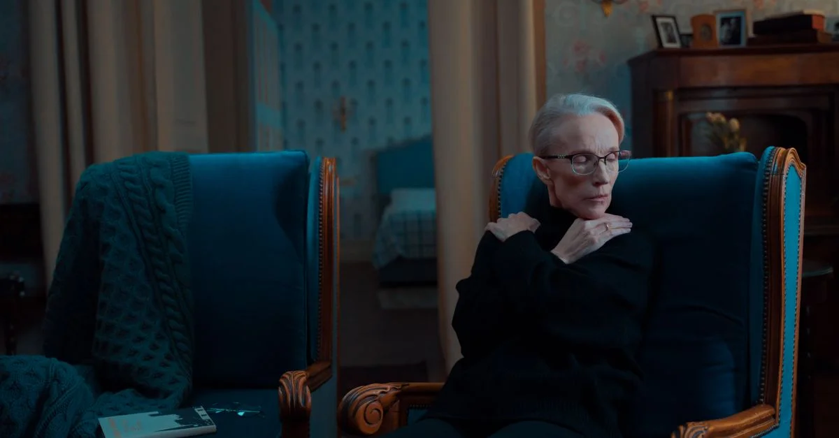 Femme senior assise dans un fauteuil vintage à l'intérieur, dégageant une atmosphère sereine et contemplative.