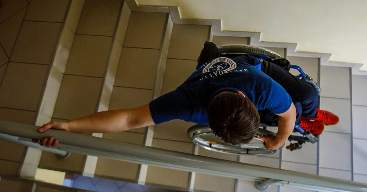 Vue aérienne d'une personne en fauteuil roulant descendant des escaliers à l'intérieur, s'accrochant aux rampes.