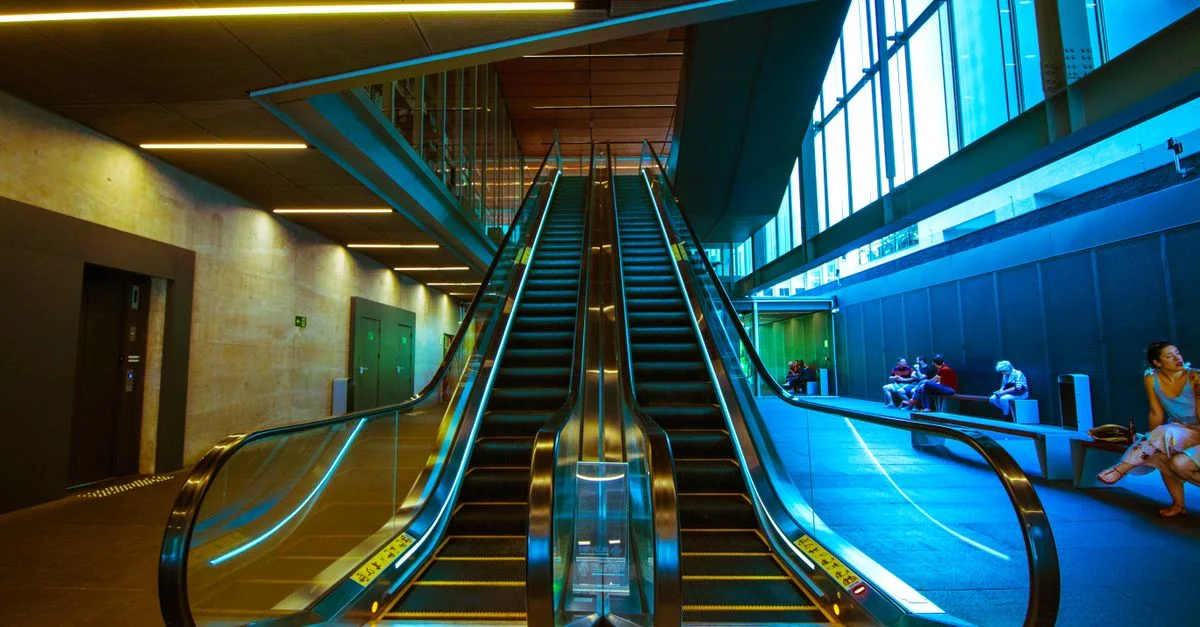 Un escalier mécanique moderne à l'intérieur d'un bâtiment urbain avec des personnes assises. Design architectural vibrant.