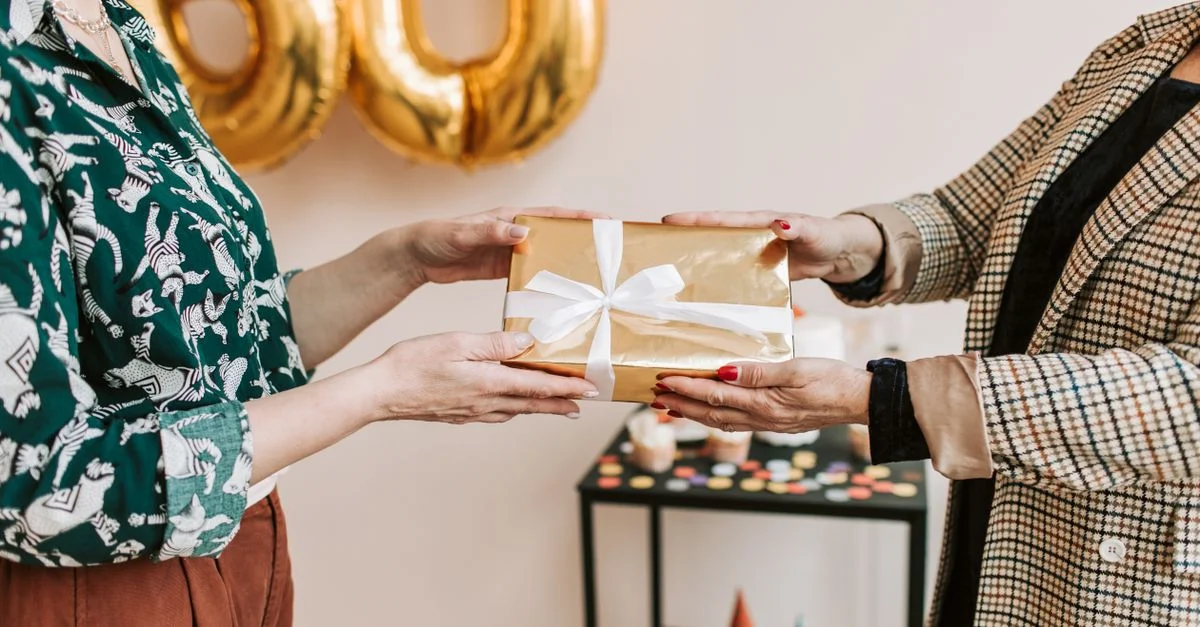 Deux personnes échangeant un cadeau emballé lors d'une célébration d'anniversaire avec des décorations en arrière-plan.