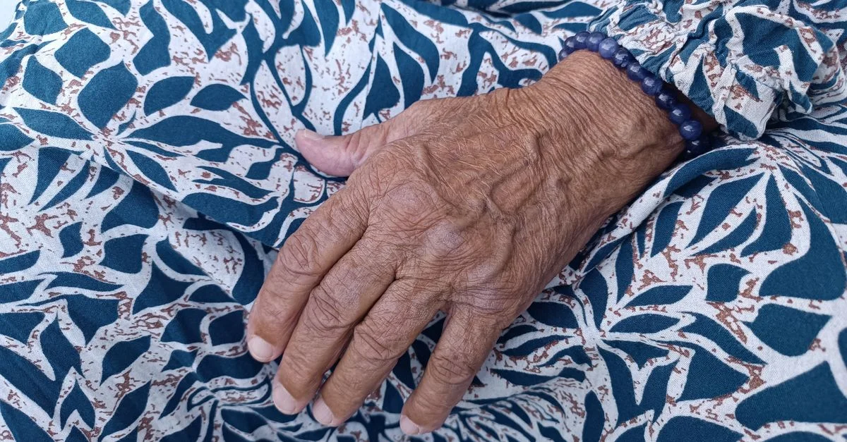 Gros plan d'une main âgée posée sur un tissu à motifs, illustrant l'âge et la texture.