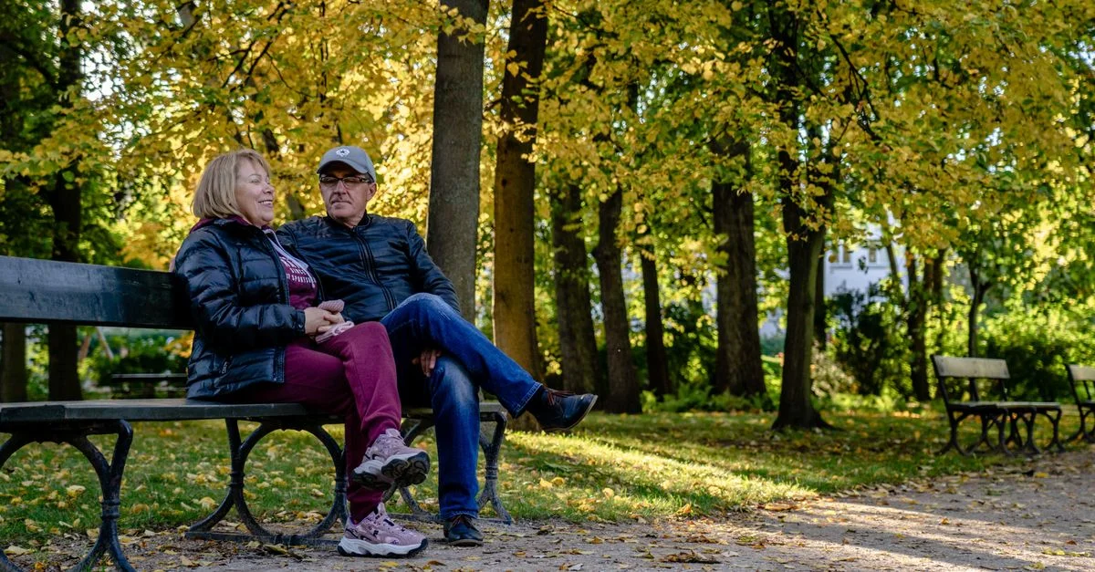 Un couple senior heureux assis sur un banc de parc entouré de feuillage automnal.