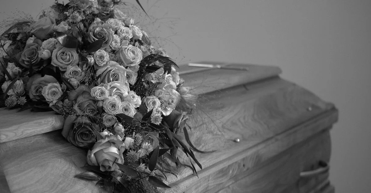 Une image en noir et blanc présentant une caisse en bois ornée d'un bouquet floral vibrant, symbolisant le respect et la mémoire.