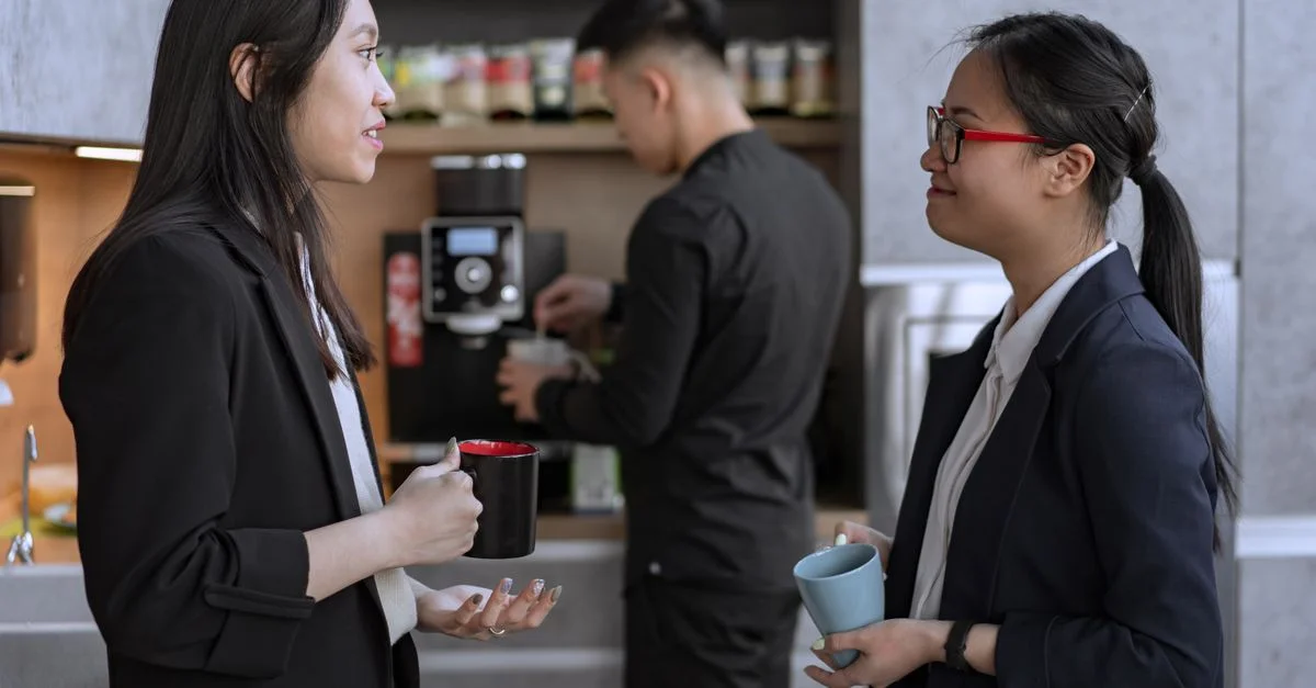 Deux collègues féminines conversant pendant une pause café dans un environnement de bureau moderne.