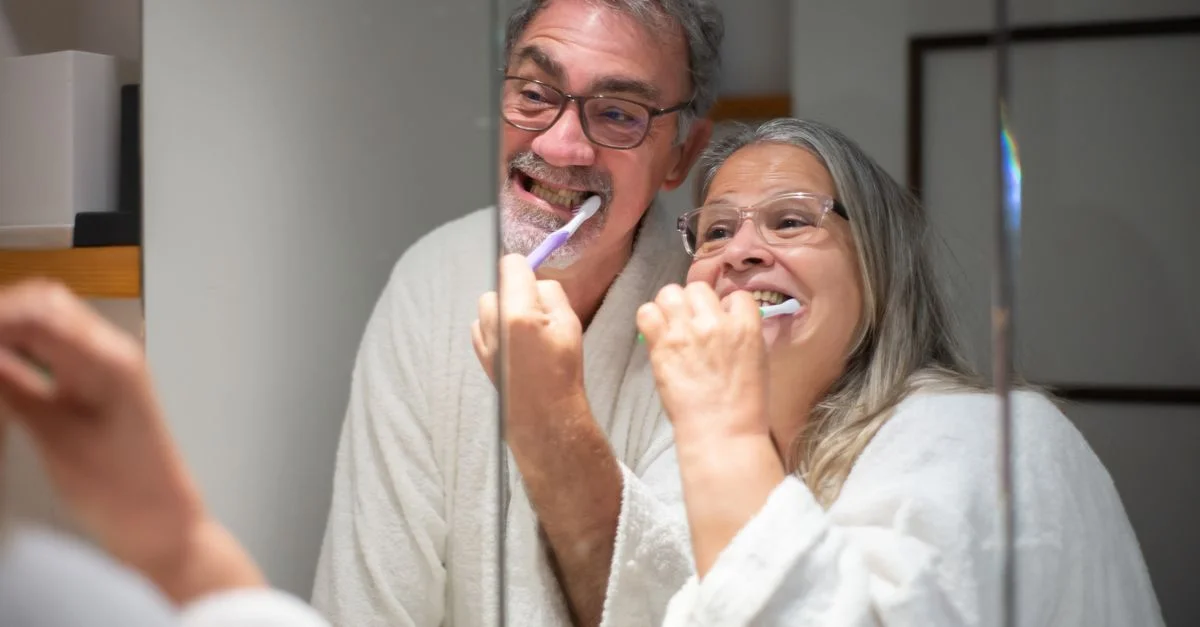 Heureux couple senior se brossant les dents ensemble devant le miroir de la salle de bains, soulignant l'hygiène dentaire.