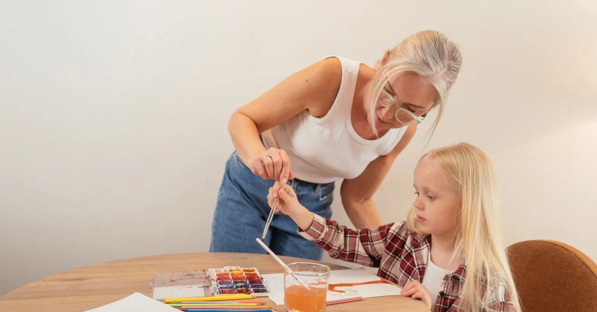 Une grand-mère guide sa petite-fille dans la peinture à l'aquarelle dans un cadre intérieur confortable.