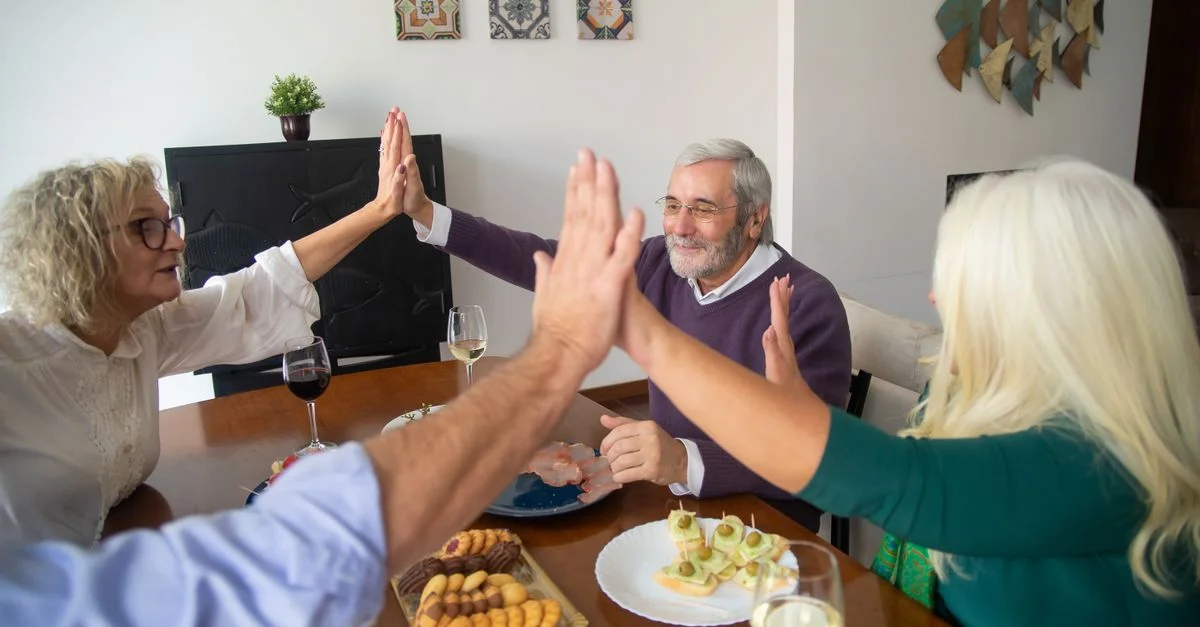 Un groupe d'amis seniors partage un dîner ensemble, s'échangeant un high five dans un cadre chaleureux et amical.