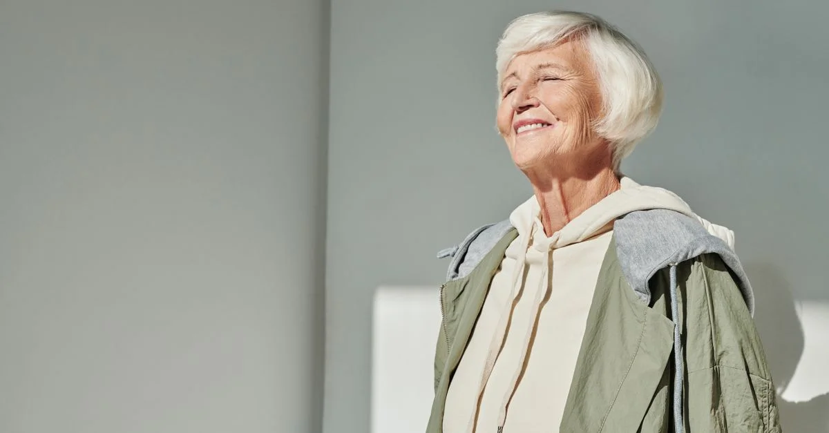 Femme senior élégante souriant au soleil, vêtue d'une tenue décontractée stylée à l'intérieur.